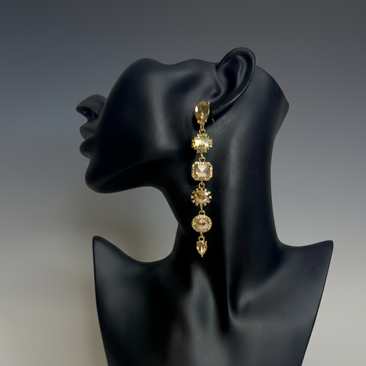 Gold strand dangle rhinestone earrings on a black mannequin ear against a gray background