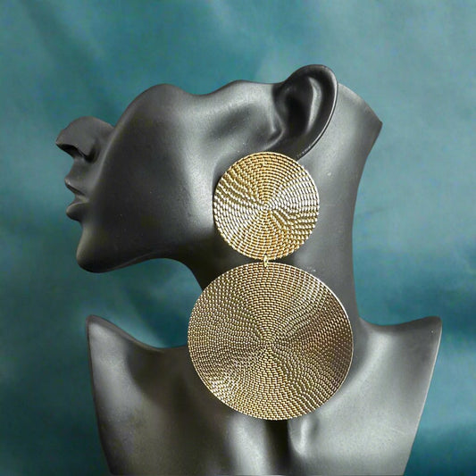A pair of gold-colored textured double metal disc dangle earrings displayed on a mannequin head.