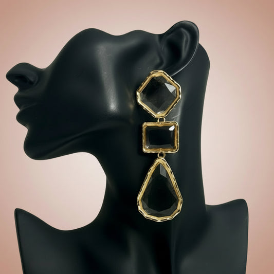 Gold geometric earrings on a black mannequin ear against a pink background