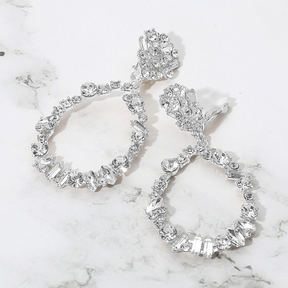 Pair of silver clip on earrings with clear gemstones on a marble surface