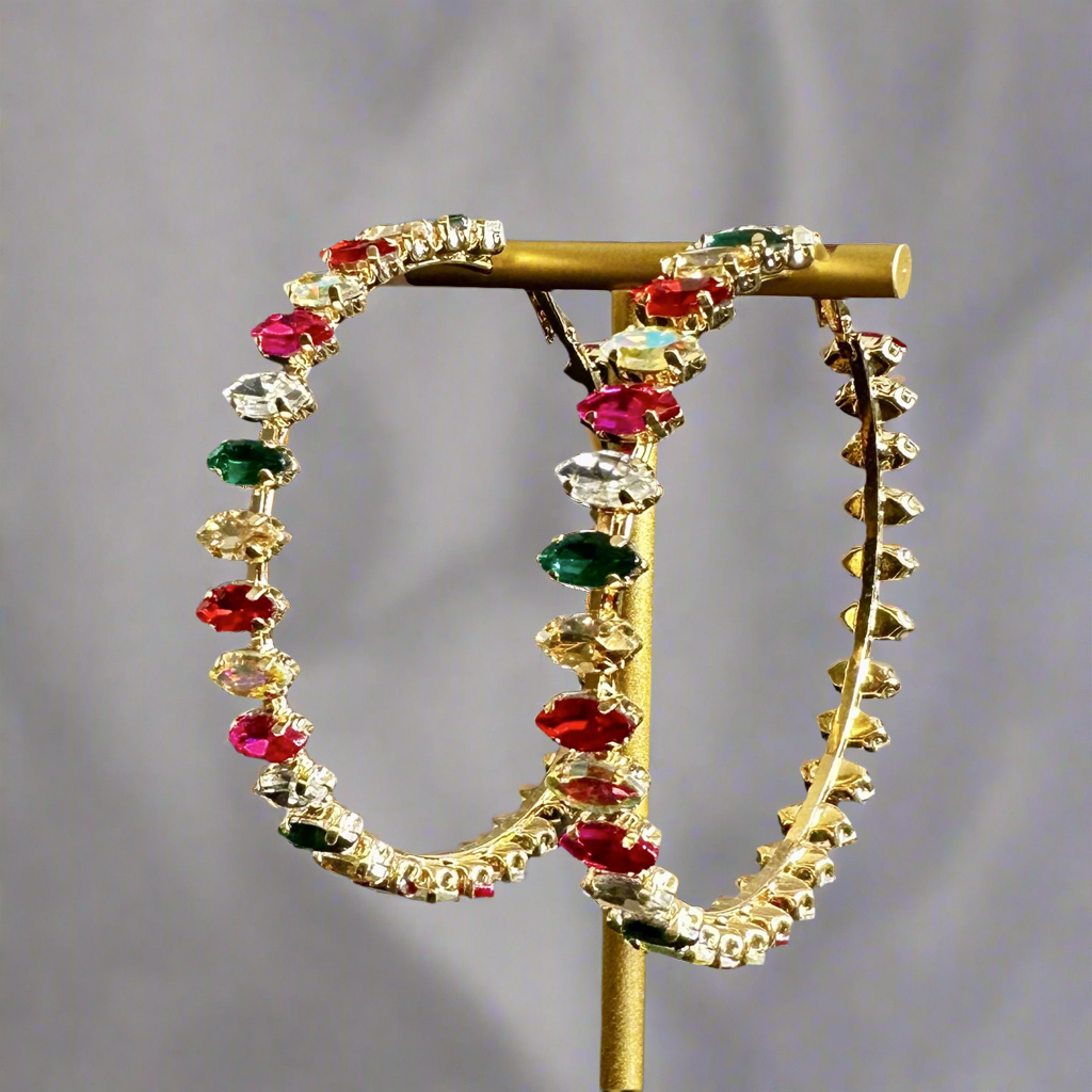 A pair of gold-colored hoop earrings embellished with multicolored crystals, displayed on a stand.