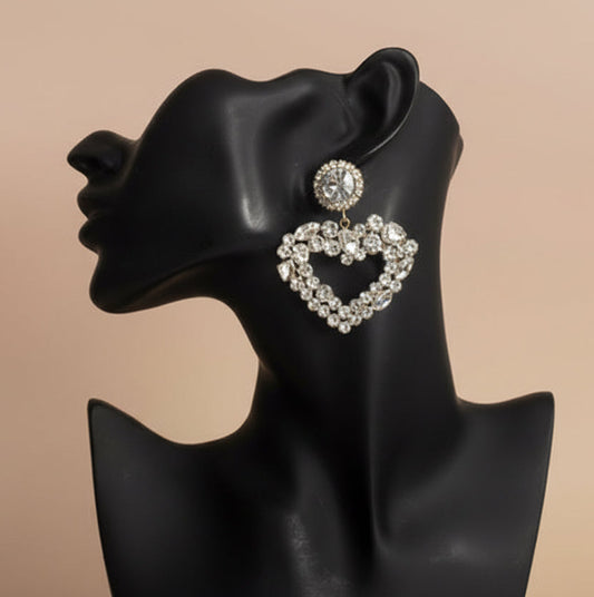 Heart-shaped rhinestone clear and gold earrings on a black mannequin bust against a beige background