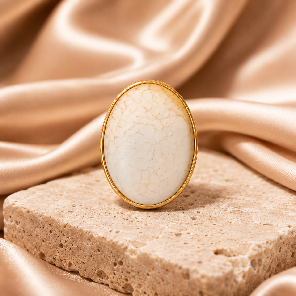 Gold ring with a white stone on a textured surface with a draped fabric background