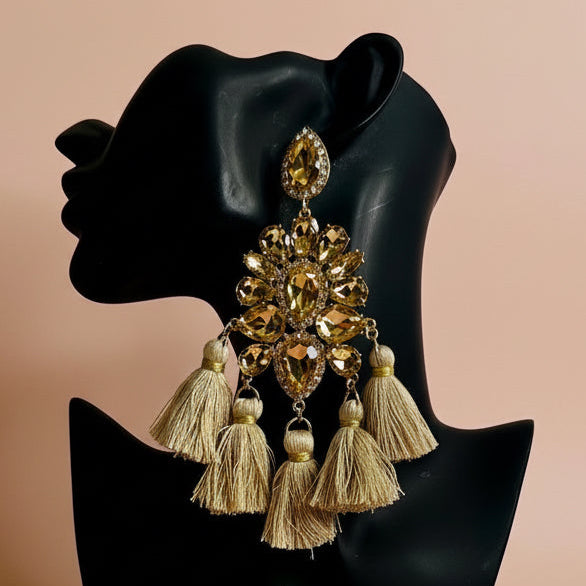 Gold earrings with tassels on a black mannequin head against a beige background