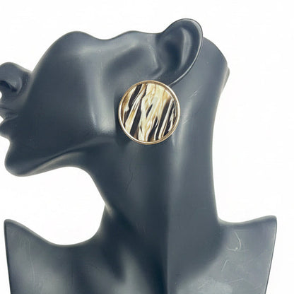 A single round gold-toned earring with a black and white zebra-like pattern, displayed on a matte dark gray female bust against a white background .