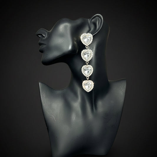 A pair of silver drop earrings with four dangling heart-shaped clear stones, displayed on a black female bust against a dark background 