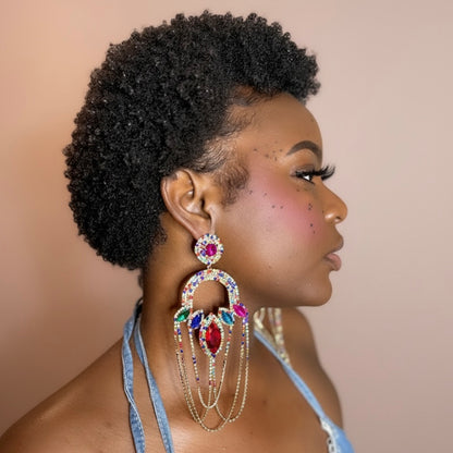 Woman with styled hair wearing colorful rhinestone dangle earrings against a beige background