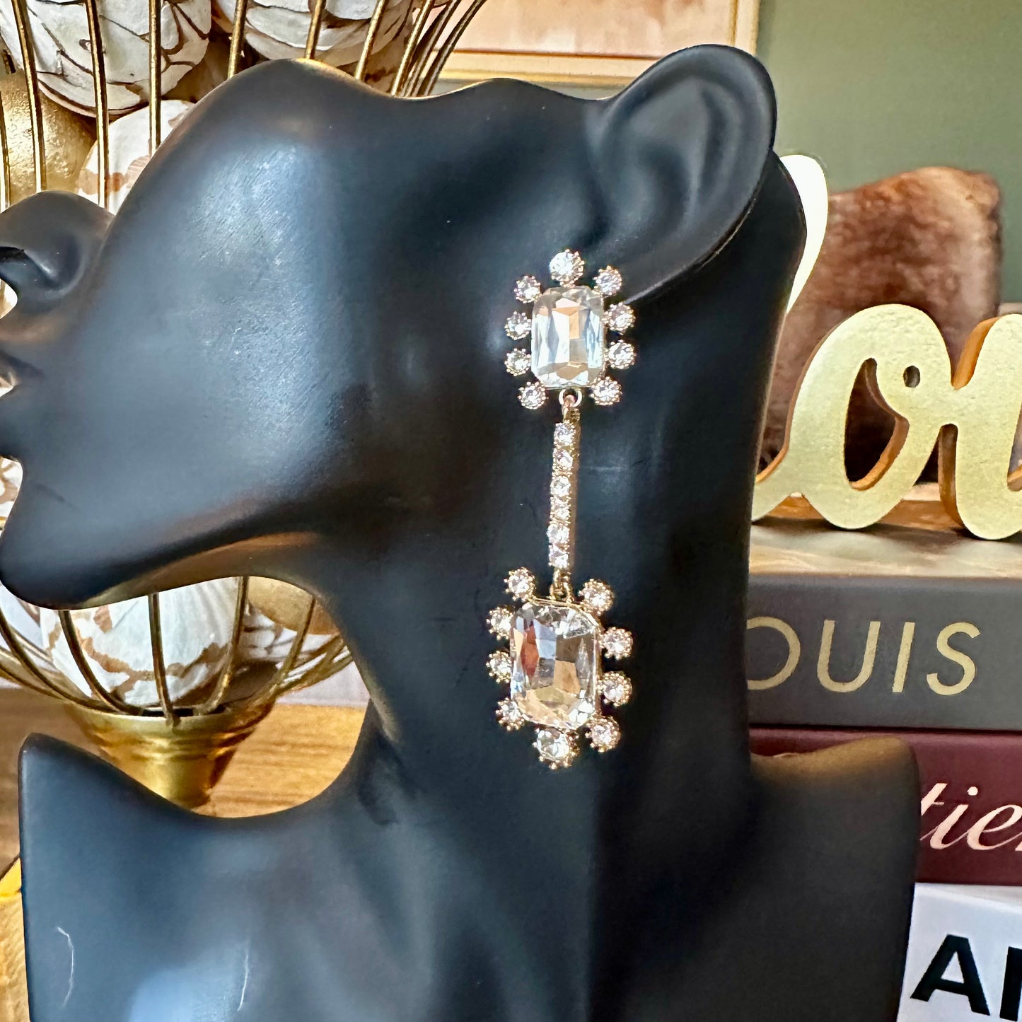 Long drop earrings featuring rectangular clear crystals framed by small round rhinestones, connected by a slim rhinestone bar, displayed on a black mannequin head.
