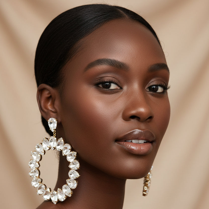 A woman wearing A pair of silver-tone hoop earrings adorned with clear rhinestones, displayed against a champagne background 