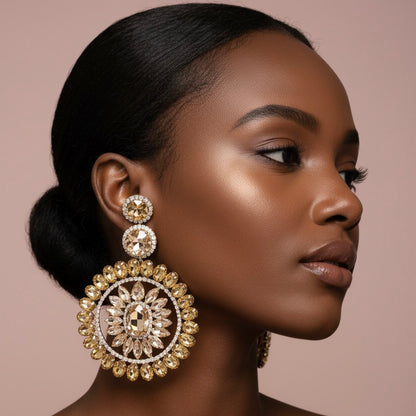 African American model wearing large gold chandelier earrings with citrine and champagne crystal sunburst design on blush nude background