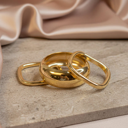 Three polished gold-colored metal bangles of varying sizes resting on a stone surface 