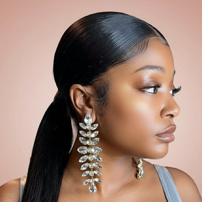 Woman wearing long, silver rhinestone dangling earrings with a plain blush background