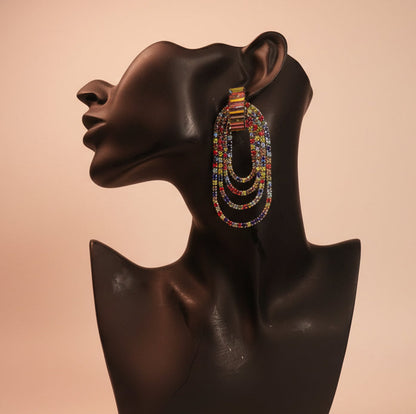 Multicolored rhinestone beaded earrings on a black mannequin head against a beige background