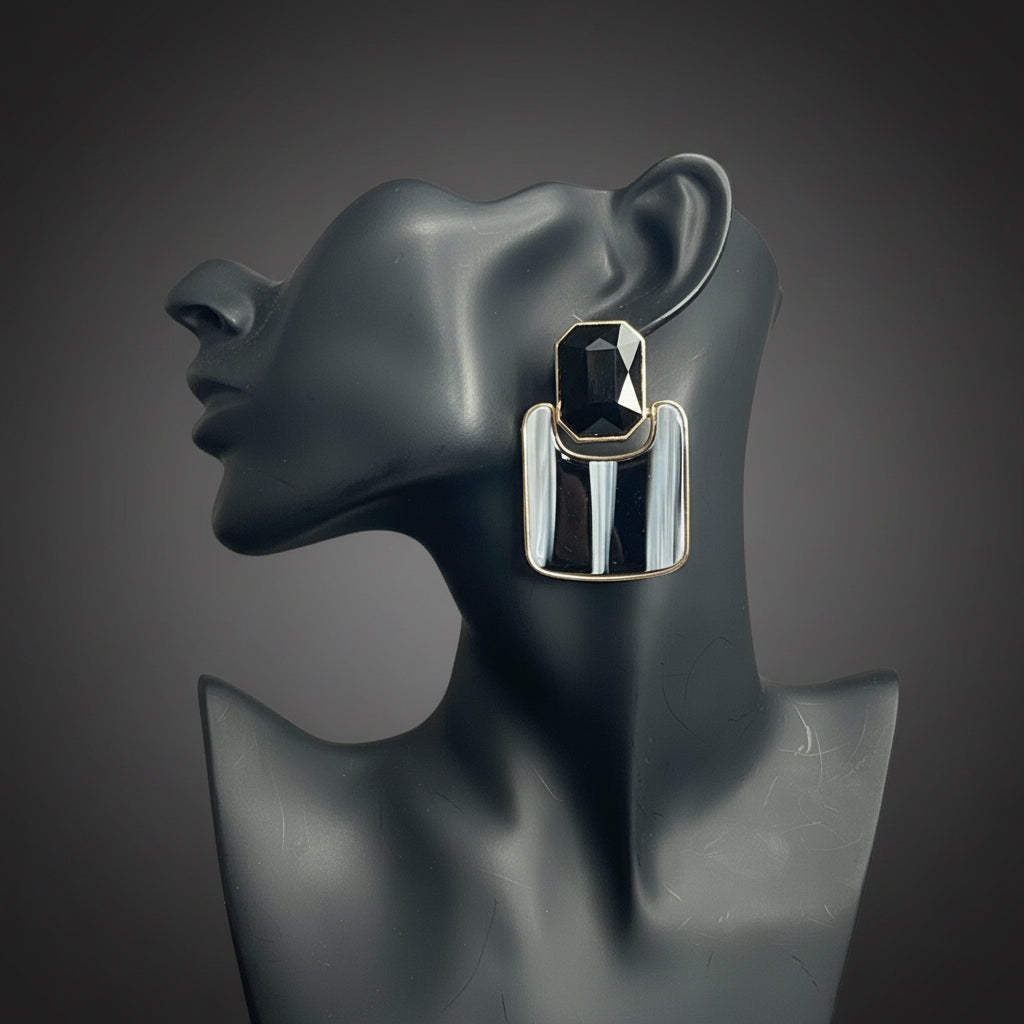 A pair of chunky silver-toned geometric drop earrings with black and white vertical stripes, displayed on a dark gray mannequin bust against a gray subway tile wall.