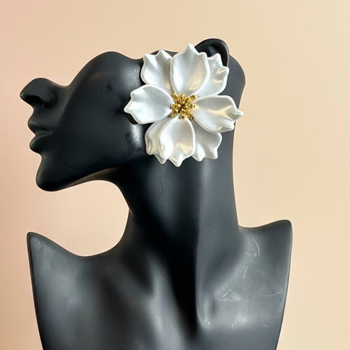 White flower-shaped earring on a black mannequin head against a beige background