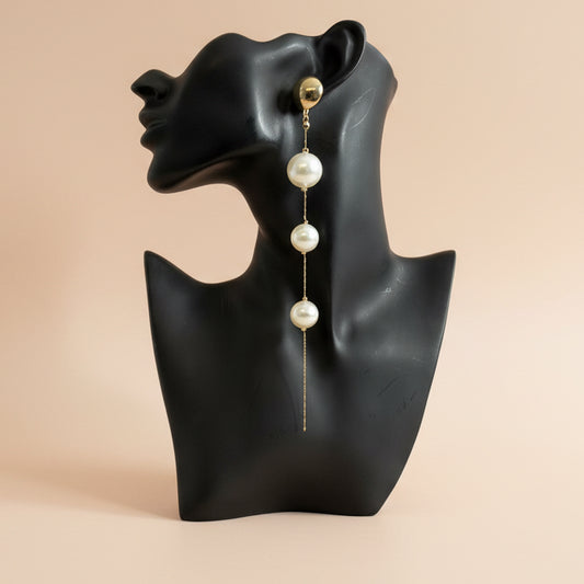 Pearl earring on a black mannequin bust against a beige background