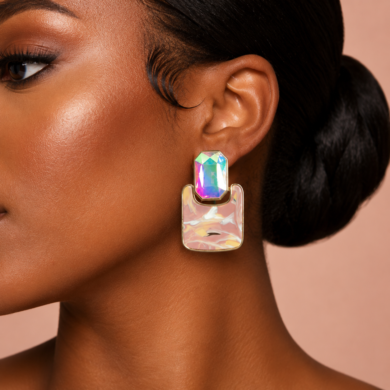 A close-up of a model's ear wearing a statement earring with an iridescent rainbow-reflecting rectangular top and a larger pearly, translucent drop below.