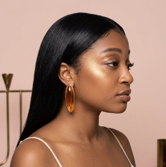 Woman with long hair wearing brown oval shaped earrings against a nude background 