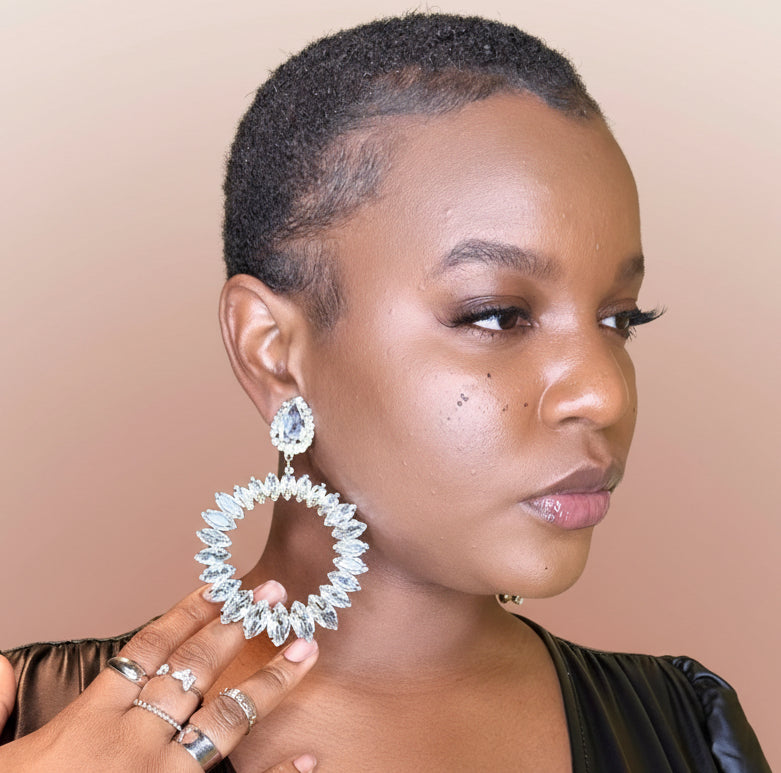 Woman wearing large Crystal Glam Statement Clip-On Earrings earrings with a blush background 