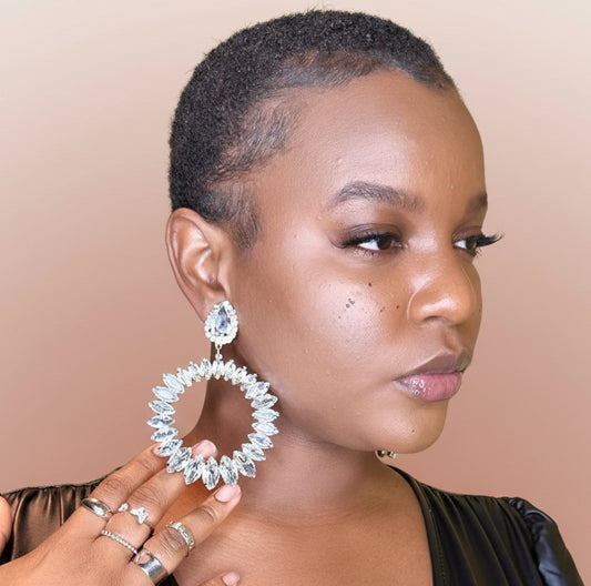 Woman wearing large Crystal Glam Statement Clip-On Earrings earrings with a blush background 