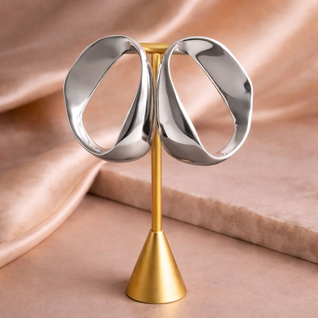 Pair of silver earrings on a gold stand against a beige fabric background