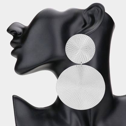 A pair of silver-colored textured double metal disc dangle earrings displayed on a mannequin head.